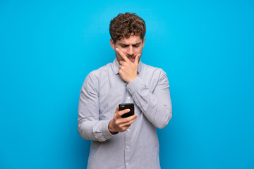 Blonde man over blue wall thinking and sending a message