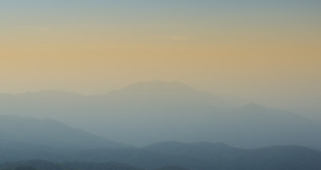 Fototapeta na wymiar Layers of mountains with orange sunset and foggy