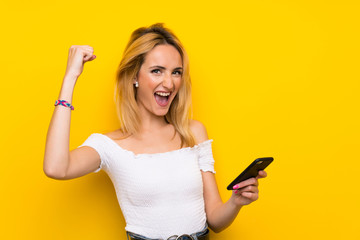 Naklejka premium Young blonde woman over isolated yellow wall using mobile phone