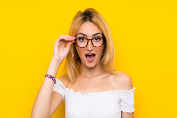 Young blonde woman over isolated yellow wall with glasses