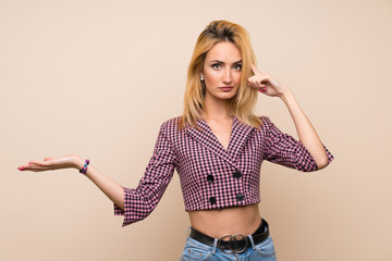 Young blonde woman with pink jacket over isolated wall making the gesture of madness putting finger...