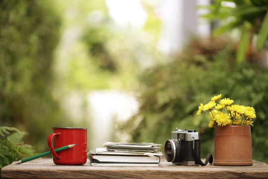 Red coffee cup with diary notebooks and vintage film camera and flower pot on wooden table - Powered by Adobe