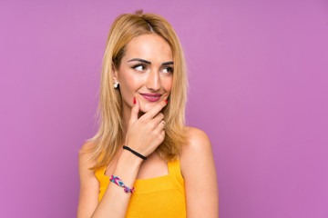 Young blonde woman over purple background thinking an idea