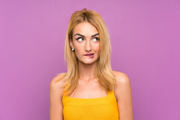 Young blonde woman over purple background having doubts and with confuse face expression
