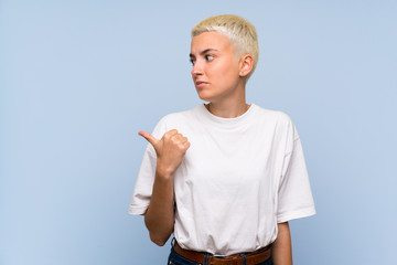 Teenager girl with white short hair over blue wall unhappy and pointing to the side