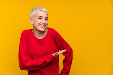 Teenager girl with white short hair over yellow wall extending hands to the side for inviting to come