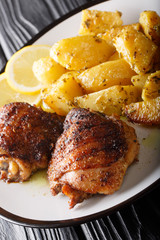 Greek lemon roasted potatoes with grilled chicken thighs on a plate close-up. vertical