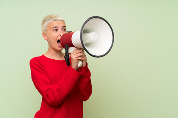 Teenager girl with white short hair over green wall shouting through a megaphone