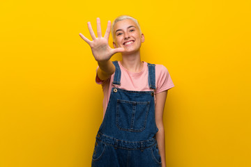 Teenager girl with overalls on yellow background counting five with fingers