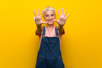 Teenager girl with overalls on yellow background counting nine with fingers