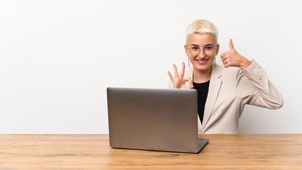 Teenager girl with short hair with a laptop showing ok sign and thumb up gesture