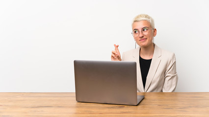 Teenager girl with short hair with a laptop with fingers crossing and wishing the best