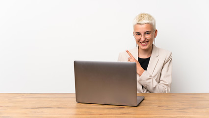 Teenager girl with short hair with a laptop pointing to the side to present a product