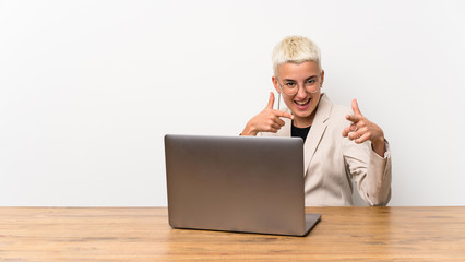 Teenager girl with short hair with a laptop pointing to the front and smiling