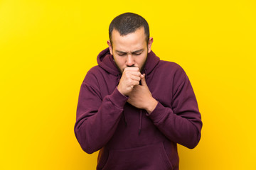 Colombian man with sweatshirt over yellow wall is suffering with cough and feeling bad