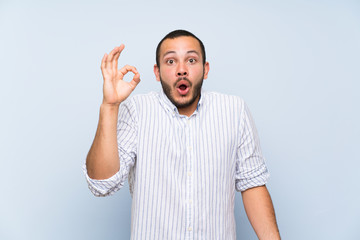Naklejka premium Colombian man over isolated blue wall surprised and showing ok sign