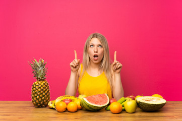 Young blonde woman with lots of fruits pointing with the index finger a great idea