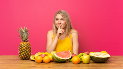 Young blonde woman with lots of fruits doing silence gesture