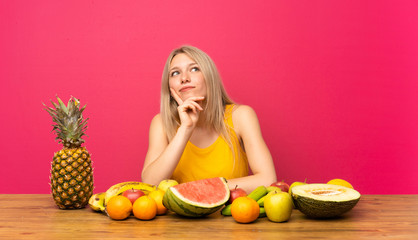 Young blonde woman with lots of fruits thinking an idea