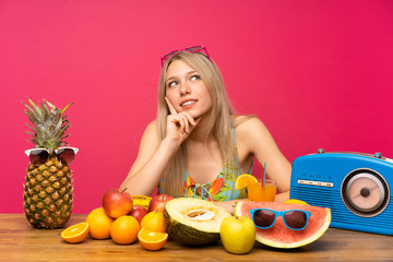 Young blonde woman with lots of fruits thinking an idea