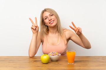 Young blonde woman having breakfast smiling and showing victory sign