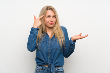 Young blonde woman over isolated white wall making the gesture of madness putting finger on the head
