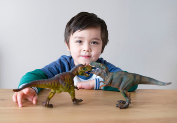 Active little boy playing with dinosaurs toys on wooden table at home, Happy child having fun play...