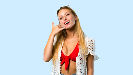 Fototapeta premium Blonde girl in summer vacation making phone gesture. Call me back sign on blue background