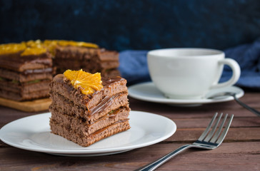 piece of chocolate cake decorated with orange slice on plate cup of tea  on wooden table soft focus