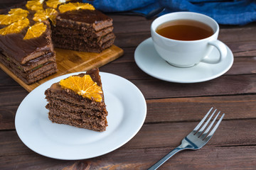 piece of homemade chocolate sponge cake  on white plate cup of tea on wooden  table