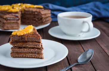 chocolate cake decorated with orange slices cup of tea  on wooden table soft focus