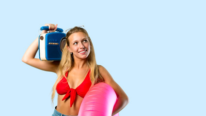 Blonde woman in summer vacation holding a radio on blue background