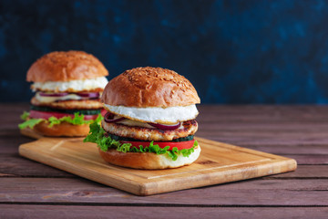 chicken burgers with fried egg lettuce tomato cheese red onion on cutting board copy space