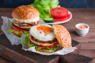 homemade burgers with chicken cutlet fried egg tomato lettuce cucumber on cutting board