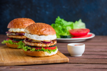 homemade chicken burgers with fried egg cucumber tomato mozzarella cheese lettuce on cutting board