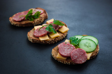 open sandwiches  rye bread sliced salami cheese and parsley on dark background  diagonal composition