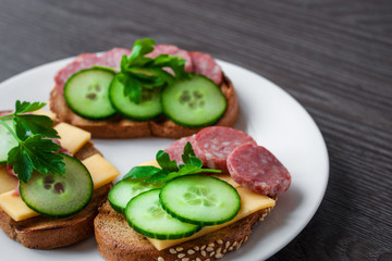 open sandwiches with salami cheese cucumber cheese parsley on white plate close up