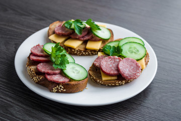 open sandwiches with salami cheese cucumber cheese parsley on white plate
