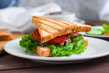 sandwich with tuna grilled bread lettuce cucumber tomato on white plate close up .healthy food 