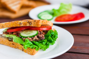 fresh sandwich with tuna tomato cucumber lettuce grilled bread  on white plate soft focus