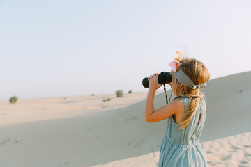 Little girl watching through the binoculars in the desert