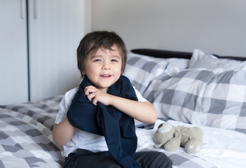 Cute boy learning how to put cloth on, 4 year old kid sitting in bed with teddy bear  wearing...