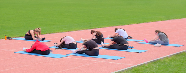 A group of young students doing yoga outdoors. Stretching girls ' backs on rubber mats in front of the gym.