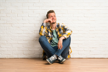 Blonde man sitting on the floor thinking an idea while looking up