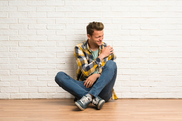 Blonde man sitting on the floor suffering from pain in shoulder for having made an effort