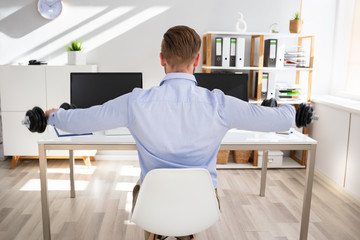 Young Businessman Exercising With Dumbbells In Office