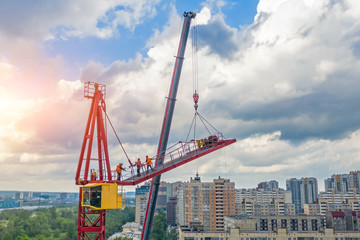 Installing the jib of a construction crane using another crane on the truck, the work of the builders of climbers at a height, fixing parts of metal structures.