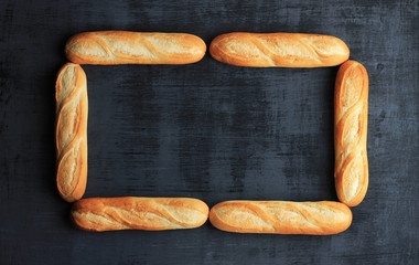 Frame made of six loafs of french baguette on black wooden background. - Powered by Adobe