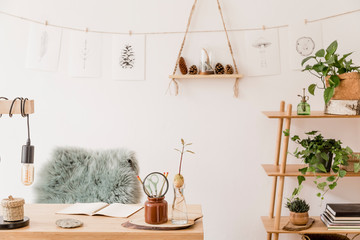 Stylish scandinavian home interior of open space, with a lot of plants, design accessories, bamboo shelf, wooden desk and hanging mock up forest drawings . Botany concept of home decor. Sunny room.