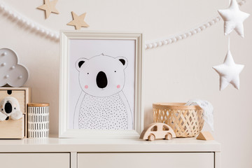 Stylish and cozy childroom with white mock up photo frame, wooden accessories, toys, clouds, rattan basket and white garland and stars on the white wall. Bright and sunny interior. Template, 